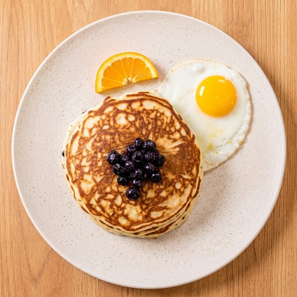 Stack of blueberry pancakes with a fried egg and orange slice on a white plate.