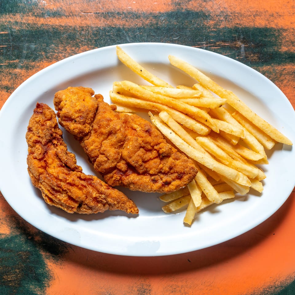 Two crispy fried chicken tenders and a pile of golden french fries on a white plate.