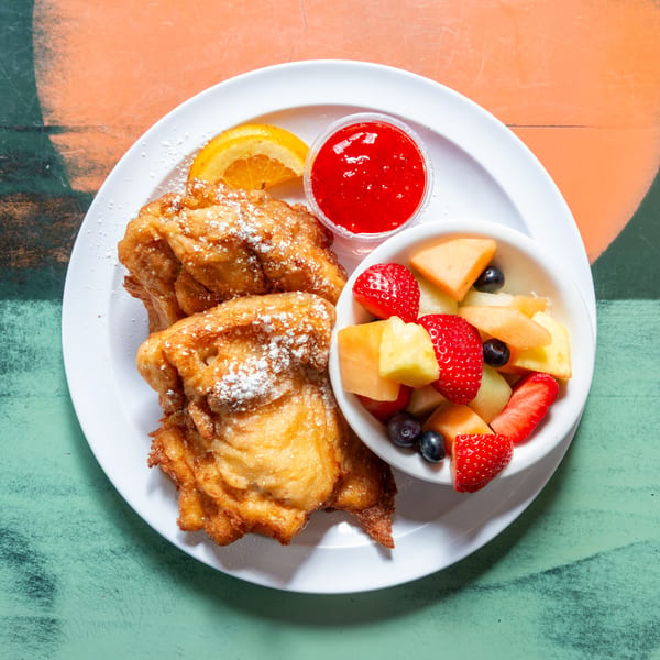 Golden-brown funnel cakes dusted with powdered sugar, served with fresh fruit and strawberry sauce.