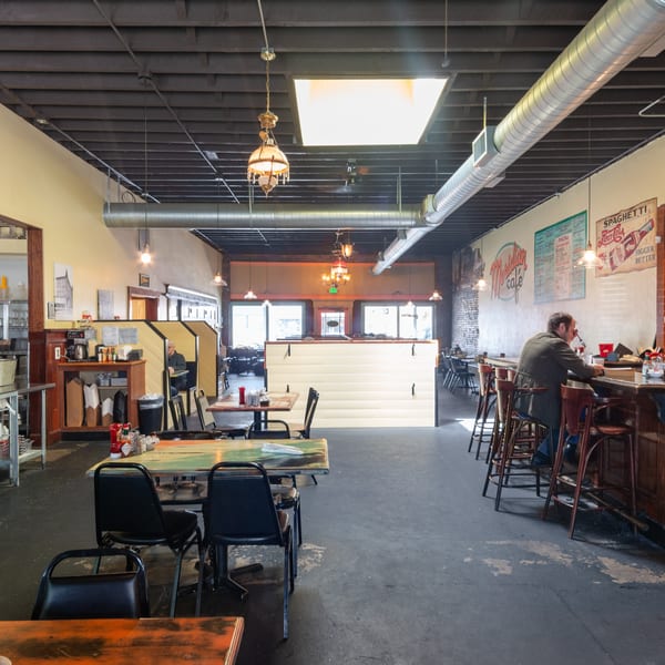 Interior of Meridian Cafe, showing dining tables, a bar with a patron, and an open kitchen area.