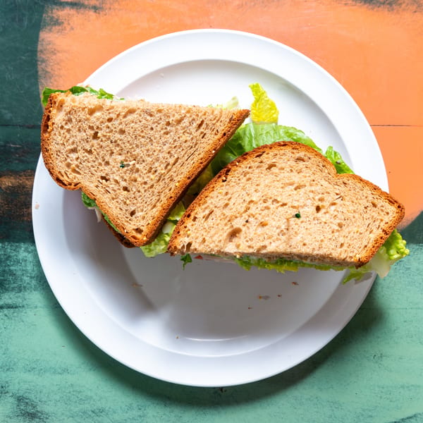 A whole wheat sandwich with lettuce and filling, cut in half, on a white plate.