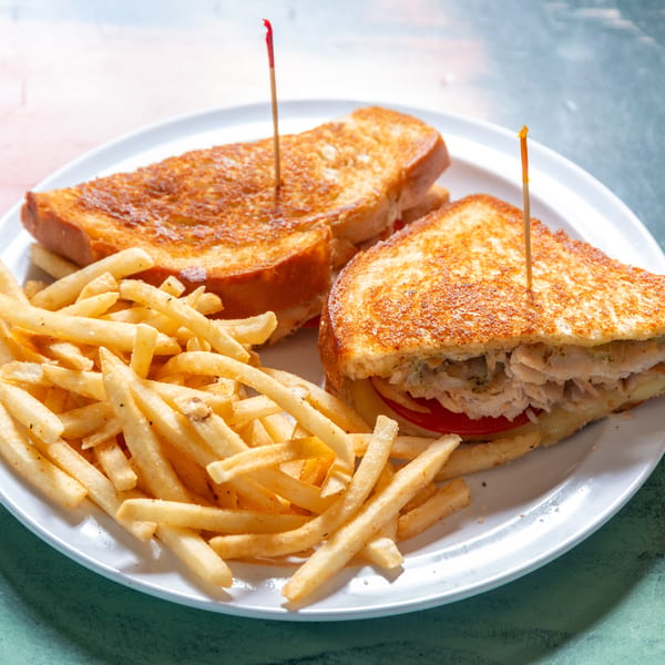 A grilled chicken sandwich with tomato and cheese, served with a side of french fries.