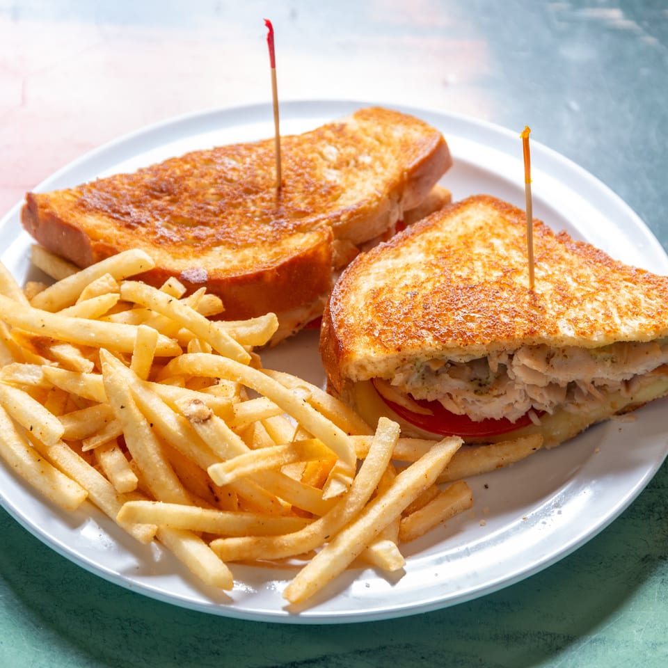 A grilled chicken sandwich with tomato and cheese, served with a side of french fries.