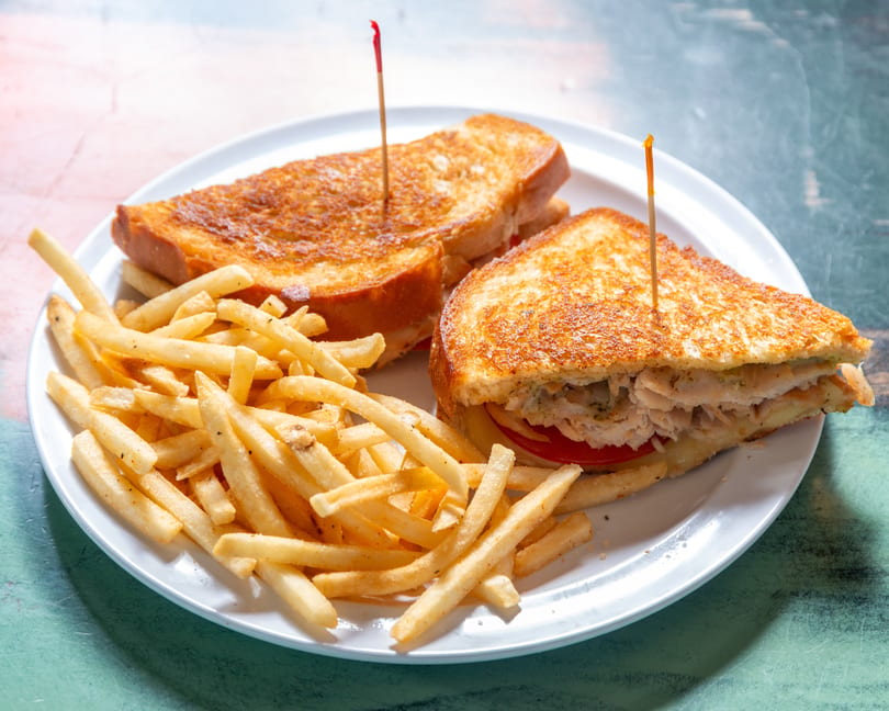 A grilled chicken sandwich with tomato and cheese, served with a side of french fries.