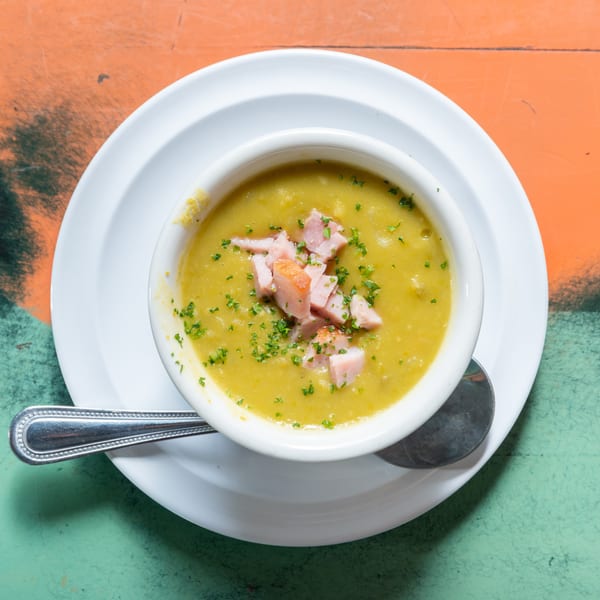 Overhead view of a white bowl of split pea soup with ham and parsley on a colorful table.