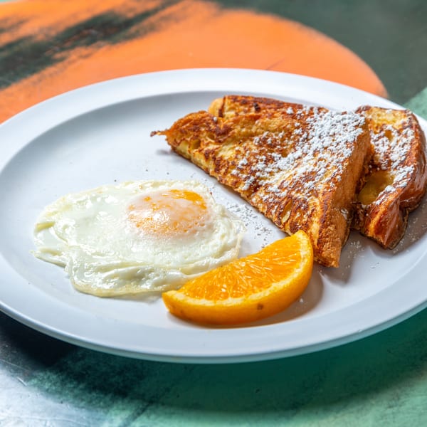 Breakfast plate with two slices of powdered sugar French toast, a fried egg, and an orange slice.