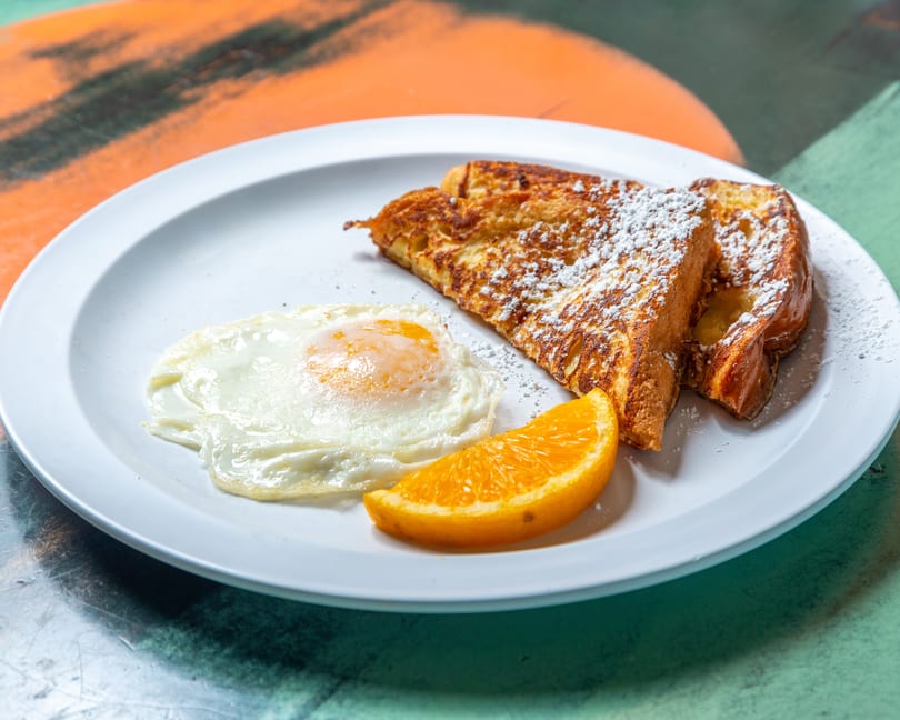 Breakfast plate with two slices of powdered sugar French toast, a fried egg, and an orange slice.