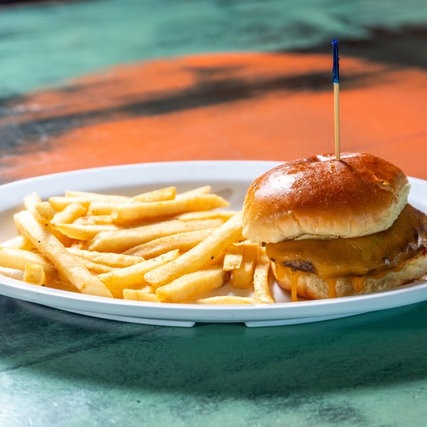 A cheeseburger with melted cheese and a side of golden french fries on a white plate.