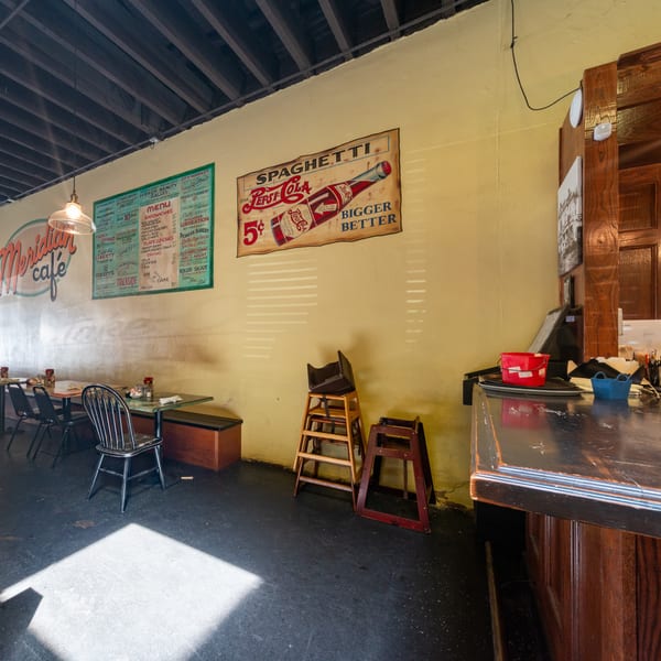 Interior of Meridian Cafe with vintage signs, tables, chairs, and a dark wooden counter.