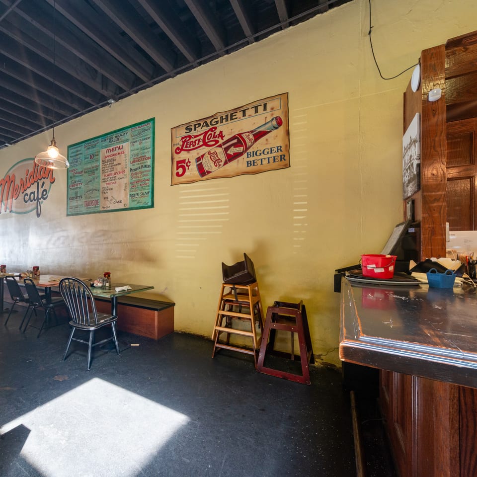 Interior of Meridian Cafe with vintage signs, tables, chairs, and a dark wooden counter.