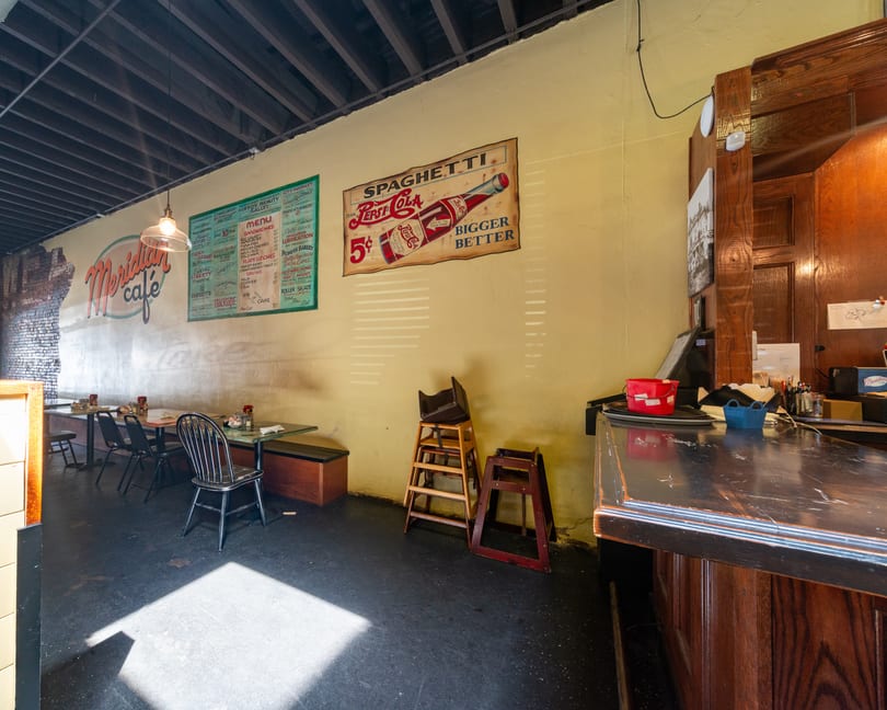 Interior of Meridian Cafe with vintage signs, tables, chairs, and a dark wooden counter.