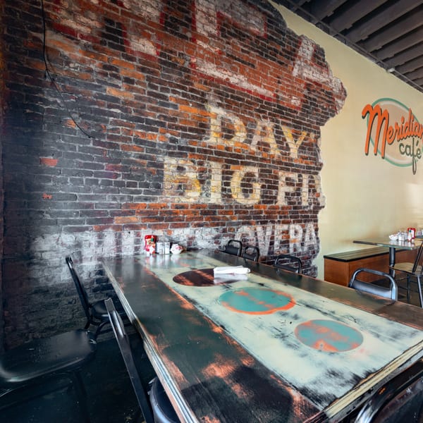 Interior of Meridian Cafe with a long distressed wooden table, brick wall, and yellow painted wall.
