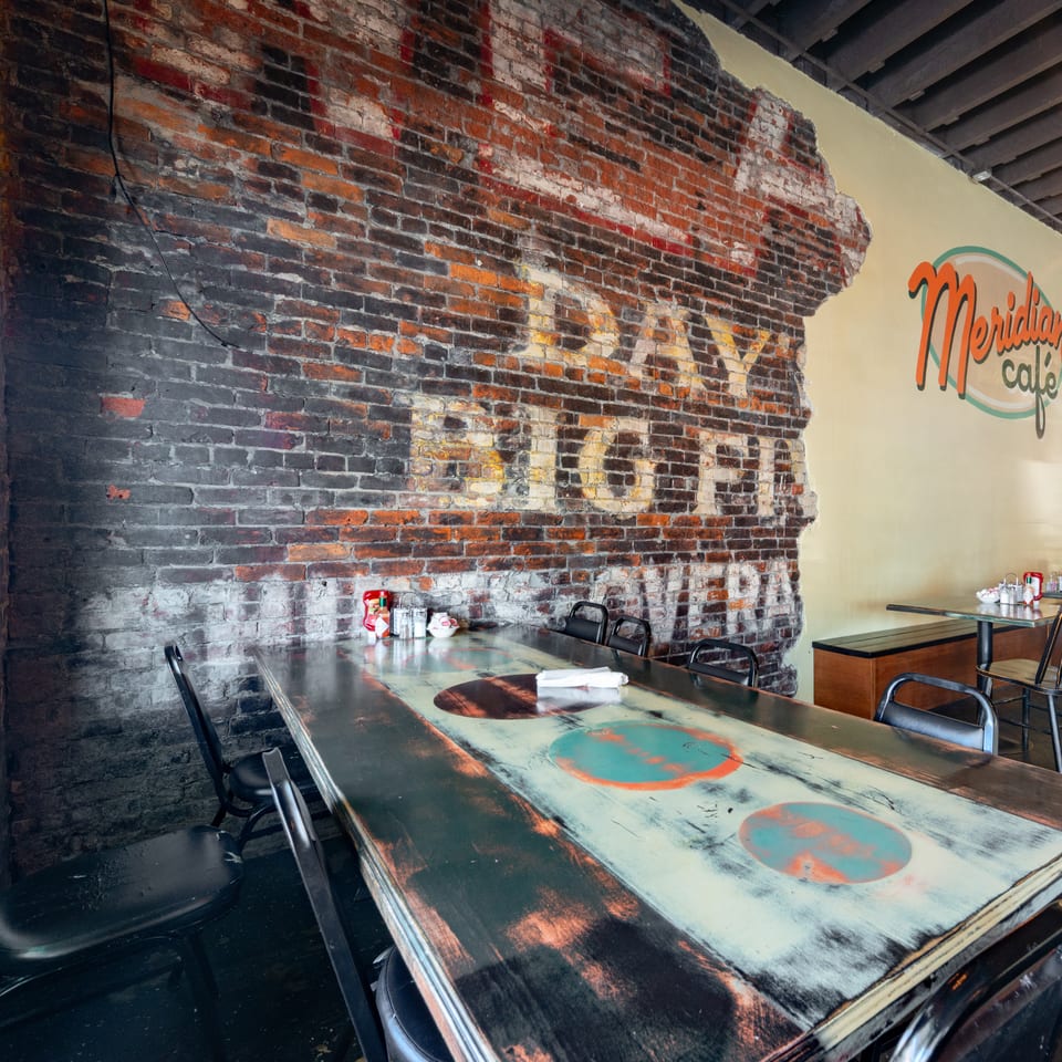 Interior of Meridian Cafe with a long distressed wooden table, brick wall, and yellow painted wall.