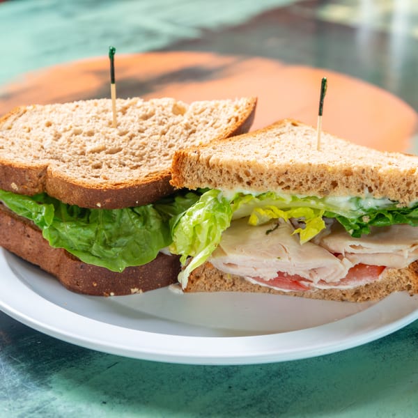 Turkey sandwich on whole wheat bread with lettuce, tomato, and mayonnaise on a white plate.