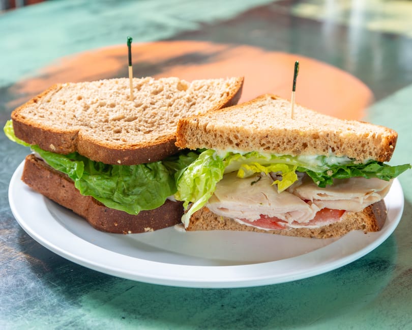 Turkey sandwich on whole wheat bread with lettuce, tomato, and mayonnaise on a white plate.