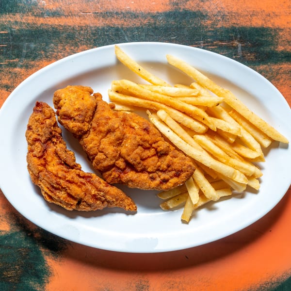 Crispy fried chicken tenders and golden french fries on a white oval plate, on a distressed orange and green table.