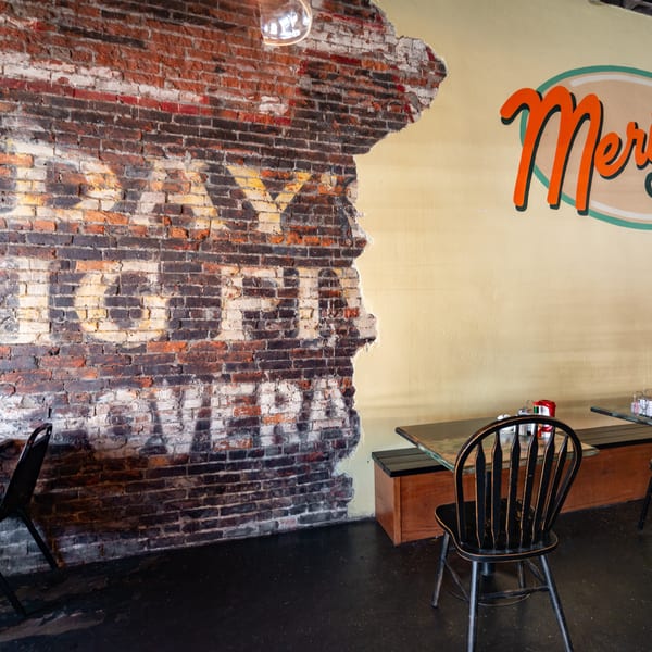 Interior of Meridian Cafe with a distressed brick wall and yellow wall with the cafe's logo.