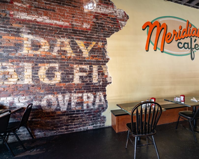 Interior of Meridian Cafe with a distressed brick wall and yellow wall with the cafe's logo.